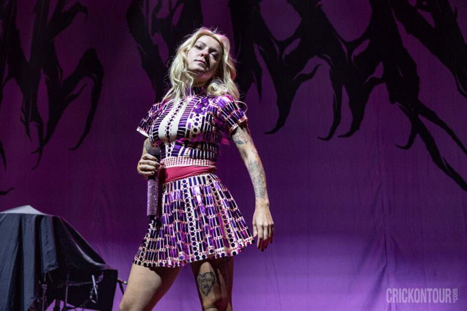 Hannah Rose Collins, lead singer stands center stage wearing a shimmering pink cowgirl dress, contrasting with the high-energy metal performance
